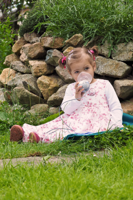 Kleines Kind, sitzend im Gras, dass inhalliert