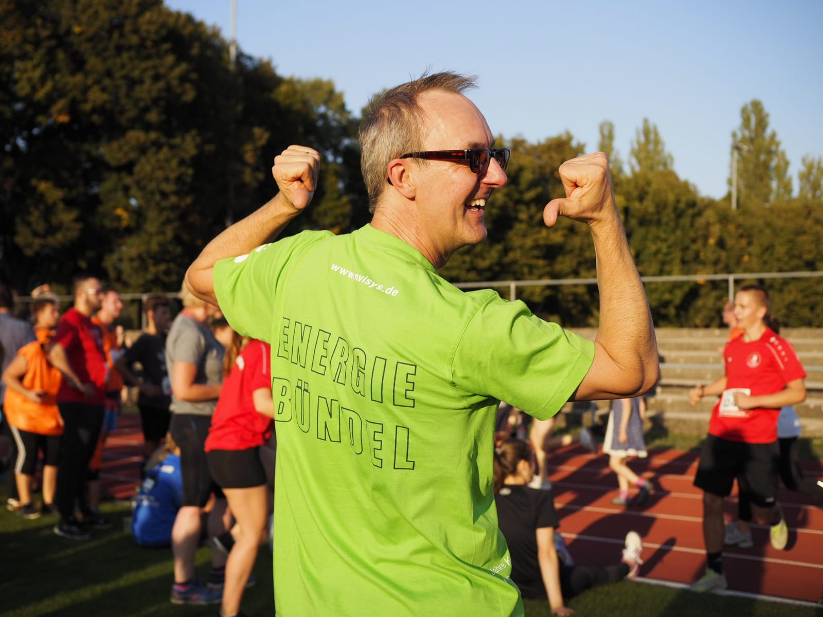 Winfried Schöffel T-Hsirt Aufschrift Energiebündel, mit den Daumen auf seinen Rücken zeigend, lachend